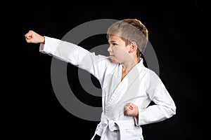 Clenched fist hit in karate, macro. Serious kid in brand new kimono on black background