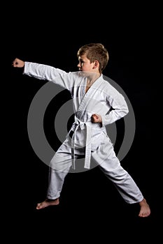 Clenched fist hit in karate. Serious kid in brand new kimono on black background