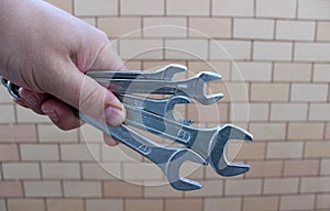 Clenched Human Fist With Different Open End Wrenches Over Brick Wall