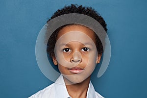 Clever black child student boy looking at camera on blue background, close up portrait