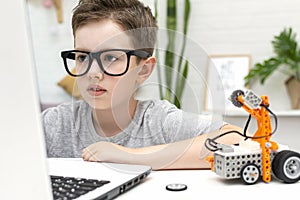 Clever boy builds and programs a robot car using a laptop at home. The child is learning coding and programming