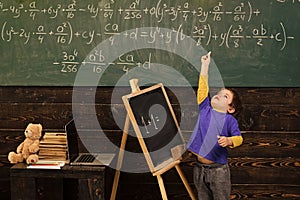 Clever boy. Tiptoeing boy pointing up with chalk in classroom. Small kid lea