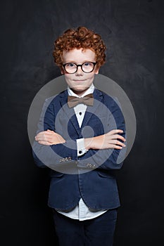 Clever child boy in glasses in classroom on chalkboard background. Smart student portrait