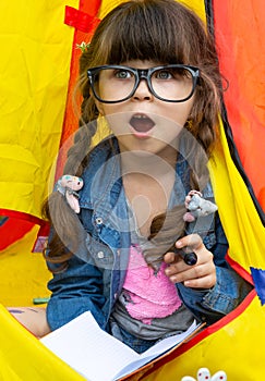 Clever child in eyeglasses holding draw and paint supplies. Kids happy to go back to school. Creative children over yellow backgro