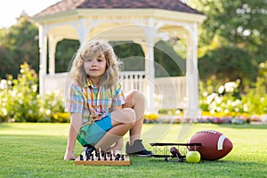 Clever concentrated and thinking kid boy playing chess. Kid playing chess and having fun outdoor on backyard or summer