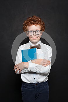 Clever kid with book on chalkboard background. Cute redhead child boy on blackboard portrait