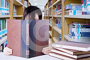 Clever little girl covered by book in the library