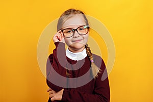 Clever little girl school girl corrects glasses. A child in a red sweater on a yellow background
