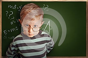 Clever pupil boy in eyeglasses near schoolboard