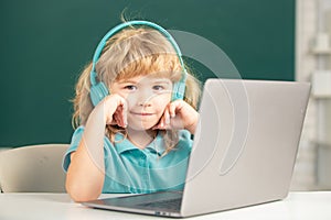 Clever school boy, cute pupil wears headphones writing on laptop, listen audio lesson use computer. Elementary school