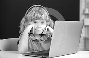 Clever school boy, cute pupil wears headphones writing on laptop, listen audio lesson use computer. Elementary school