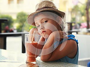 Clever serious kid girl drinking vitamin smoothie juice in street cafe and looking