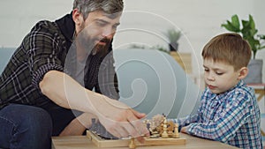 Clever small boy is playing chess with his caring father touching chesspieces and moving chessmen. Intellectual game