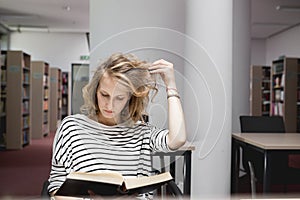 Clever student with open book reading it in college library