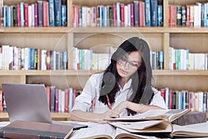 Clever teenage girl doing assignment in the library photo