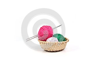Clews of different colours and knitting needles in wicker basket isolated on white background