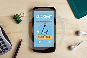Clickbait concept on smart phone screen on wooden desk