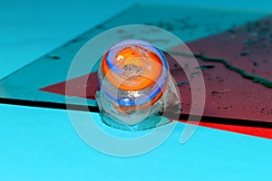 a clicker to get rid of an ice cube in which it was frozen on glass on a blue and red background