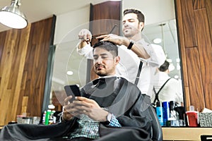Client Using Smartphone While Hairdresser Giving Him A Haircut