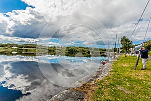 Clifden harbor at high tide with anchored boats and clouds that are reflected in the water with a tourist taking a picture