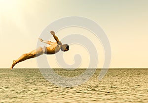 Cliff diver jumping in the sea against the sky at sunset