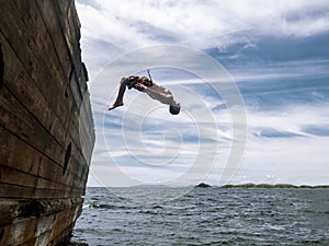 Cliff jumping: A young guy in shorts jumps into seawater from the side of an old ship.