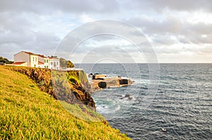 Cliffs by the Atlantic ocean in fishermans village Lagoa, Sao Miguel Island, Azores, Portugal. Traditional houses on the