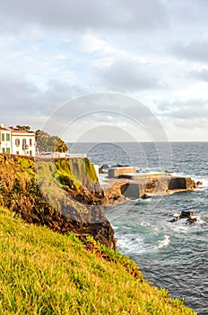 Cliffs by the Atlantic ocean in fishermans village Lagoa, Sao Miguel Island, Azores, Portugal. Traditional houses on the