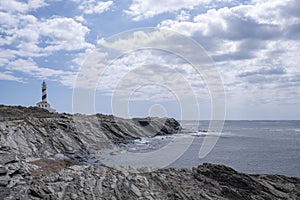 cliffs of Favaritx lighthouse, with a rock formation around it and the mediterranean sea with waves on a cloudy summer day,