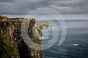 Cliffs of Moher surrounded by the sea under a cloudy sky and sunlight in Ireland