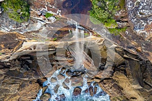 Clifftop woman sitting by the edge of waterfall tumbling into ocean