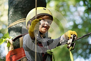 Climber child on training. Cute little boy in climbing safety equipment in a tree house or in a rope park climbs the