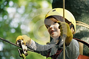 Climber child on training. Cute little boy in climbing safety equipment in a tree house or in a rope park climbs the