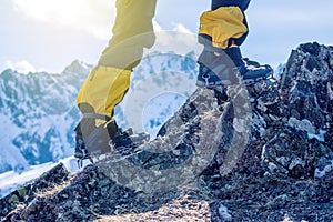 Climber in crampons stands on the rocks in front of the entrance to the peak on the background of the snowy mountains.