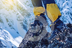 Climber in crampons stands on the rocks in front of the entrance to the peak on the background of the snowy mountains.