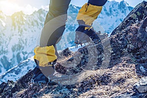 Climber in crampons stands on the rocks in front of the entrance to the peak on the background of the snowy mountains.