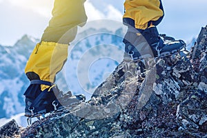 Climber in crampons stands on the rocks in front of the entrance to the peak on the background of the snowy mountains.