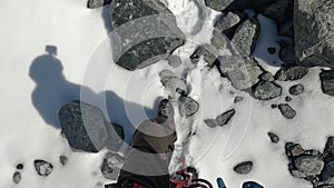 A climber with full equipment walks along a snowy path past rocks. View of the legs.