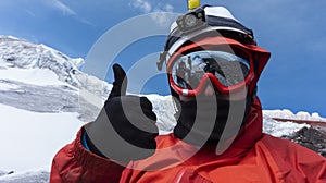 Climber with helmet, headlamp and black jacket taking a selfie on a glacier, landscape reflected in red framed glasses
