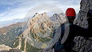 Climber man in a helmet on the top of a mountain looking into the horizon view from the back