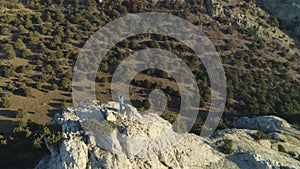 Climber man is standing on top of rock and raising hands victoriously. Aerial View