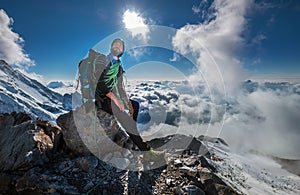 Climber in a safety harness, helmet, and high mountaineer boots with picturesque clouds background sitting at 3600m altitude on