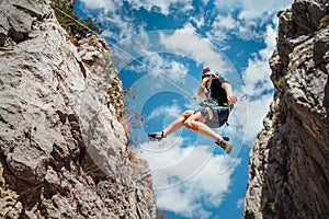 Climber teenage boy in protective helmet jumping on vertical cliff rock wall using rope Belay device, climbing harness in