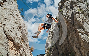 Climber teenager boy in protective helmet abseiling from vertical cliff rock wall using rope Belay device, climbing harness in photo