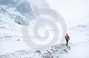 Climber walks alone in high mountains at windy snowy weather