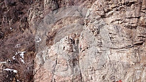 Climbers climb the rock. Drone footage. Side and top view. Rock lesson in the highlands. Gray rocks and dry bushes. Sometimes ther