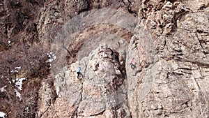 Climbers climb the rock. Drone footage. Side and top view. Rock lesson in the highlands. Gray rocks and dry bushes. Sometimes ther