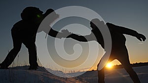 Climbers help friend climb stretch of helping hand. two tourists at top of mountain. Silhouette of travelers in winter