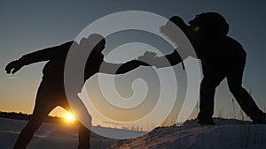 Climbers help friend climb stretch of helping hand. two tourists at top of mountain. Silhouette of travelers in winter