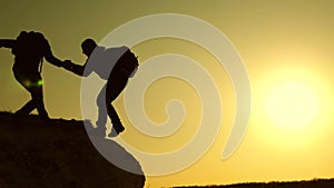 Climbers silhouettes stretch their hands to each other, climbing to the top of the hill. travelers climb one after